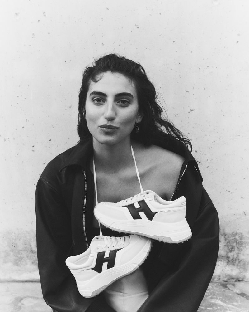 Black and white portrait of a model holding white sneakers with dark H logos for the Hogan S/S 2025 campaign.