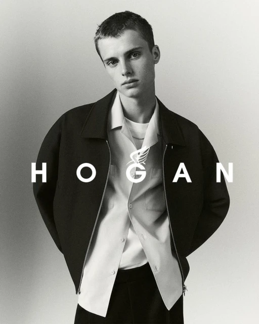 Monochrome portrait of a young male model in a dark zip jacket and white collared shirt against a neutral background.