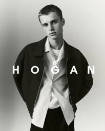 Monochrome portrait of a young male model in a dark zip jacket and white collared shirt against a neutral background.