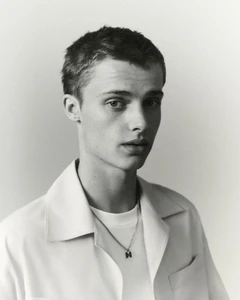 Portrait of a young male model wearing a white shirt and a pendant necklace against a plain light background