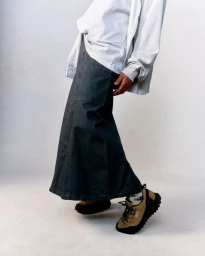 Model wearing a grey long skirt, white hoodie, and patterned trail shoes against a neutral background