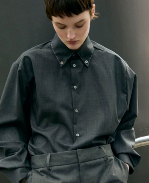 Model wearing a dark grey button-down shirt and matching trousers against a dark background.