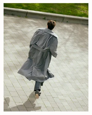 Person seen from behind running on a paved stone pathway wearing a long grey belted coat.