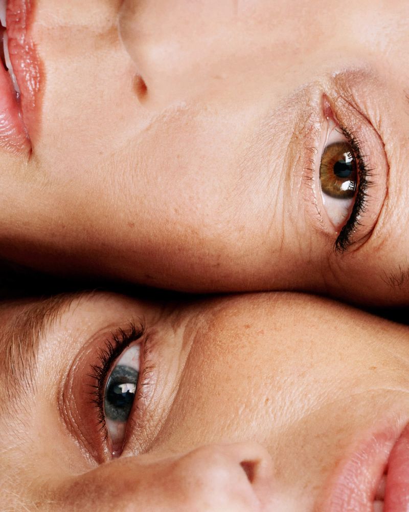 Close-up studio portrait of two adult females with light skin and different-colored eyes, illuminated by soft lighting.