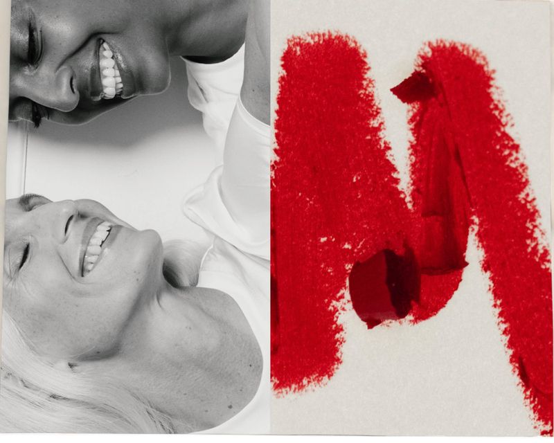 Black and white portrait of two smiling women with red lipstick smear on adjacent white surface, creating a vibrant and contrasting image.