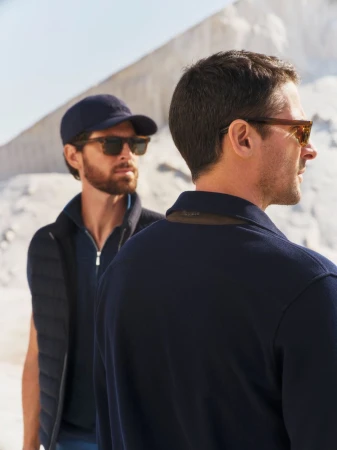 Two adult men in casual outfits and sunglasses stand against a bright white landscape. Fashion and style in an outdoor setting.