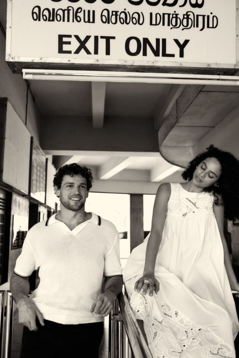 Monochrome shot of a smiling man and a woman in a white dress posing in front of an 'Exit Only' sign, creating a vintage editorial feel.