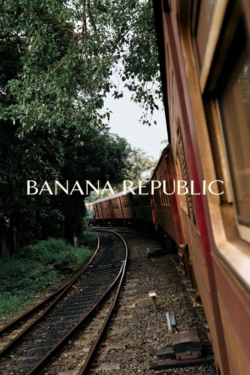 Banana Republic branded freight train on tracks, surrounded by green trees and shrubs. Train car is red, tracks are metal.