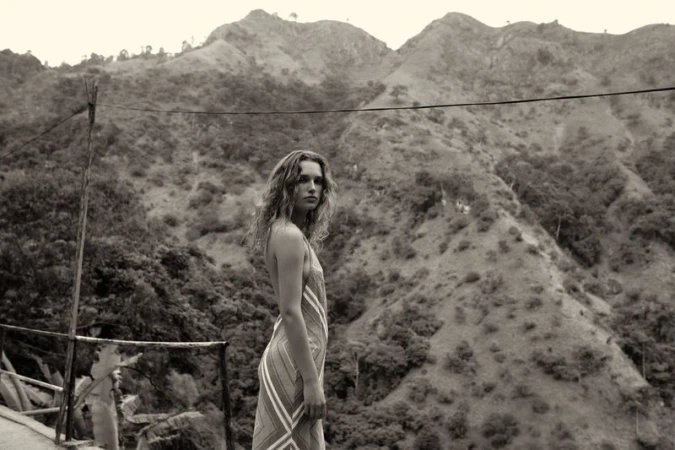 Woman in dress stands in front of mountainous landscape with lush greenery in monochrome image, creating a natural, scenic view.