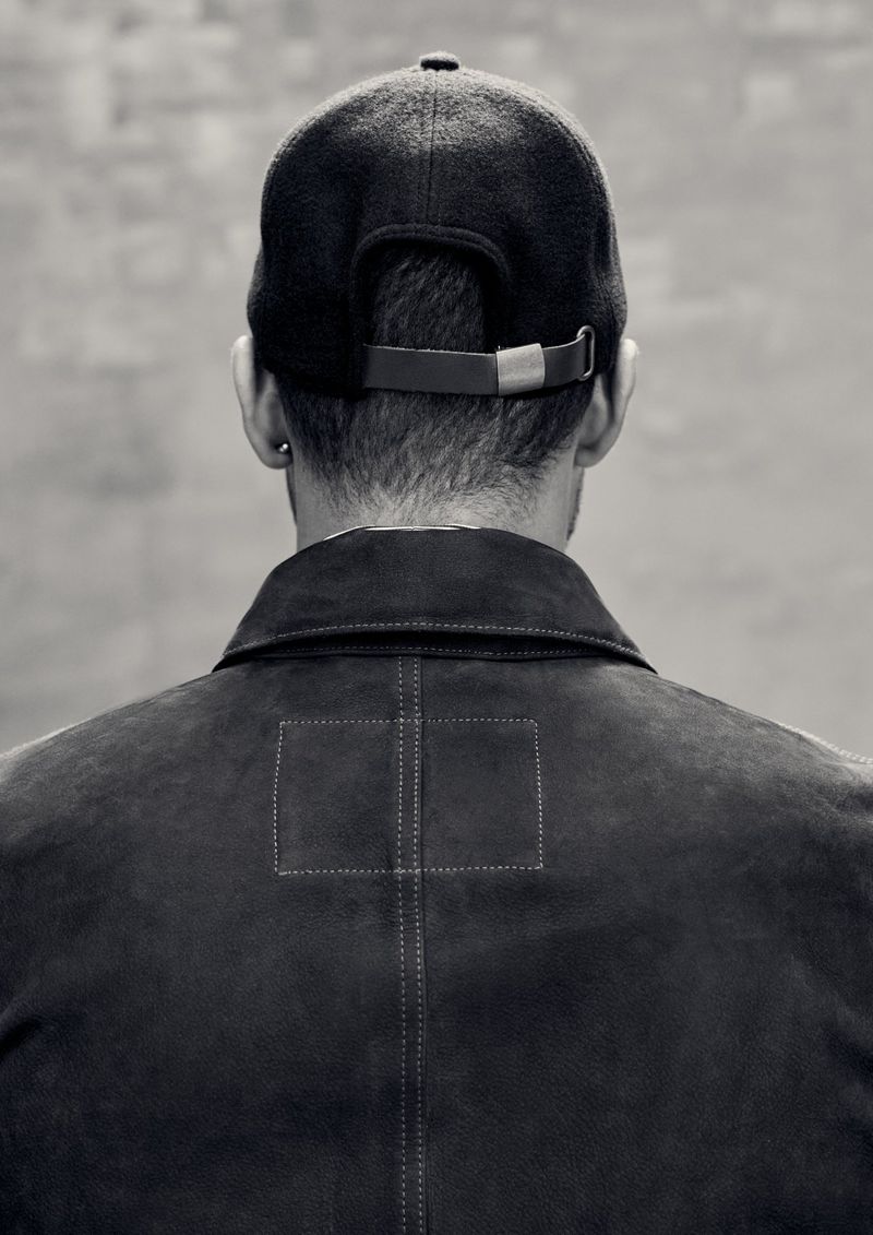 Monochrome shot from behind of adult male with baseball cap and jacket, showcasing fashion and neutral tones.