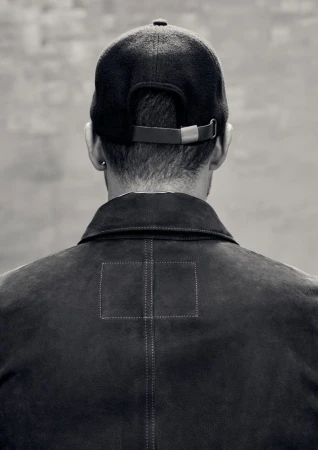 Monochrome shot from behind of adult male with baseball cap and jacket, showcasing fashion and neutral tones.