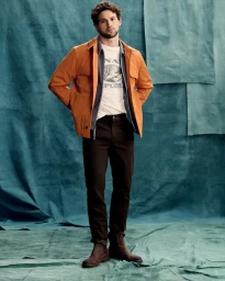 Giacomo Cavalli wearing an orange jacket and dark trousers against a teal textured backdrop for Banana Republic Spring 2025