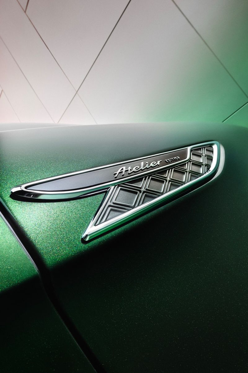 Close-up of an automotive emblem with 'Atelier' inscription on a green car surface, showcasing design details and texture.