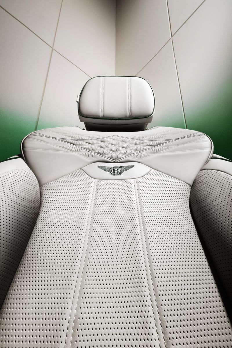 Close-up studio shot of a white Bentley car seat featuring perforated leather, diamond stitching, and the Bentley logo centered on the upper seat.