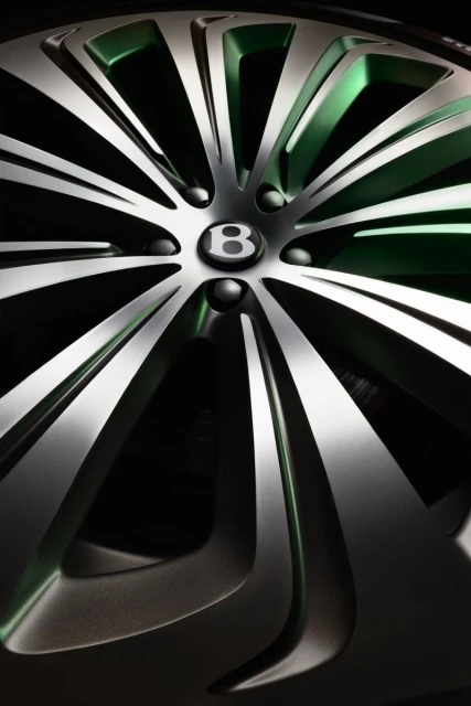 Close-up shot of a Bentley car wheel with a silver and green finish, showcasing the elegant design and iconic 'B' logo.