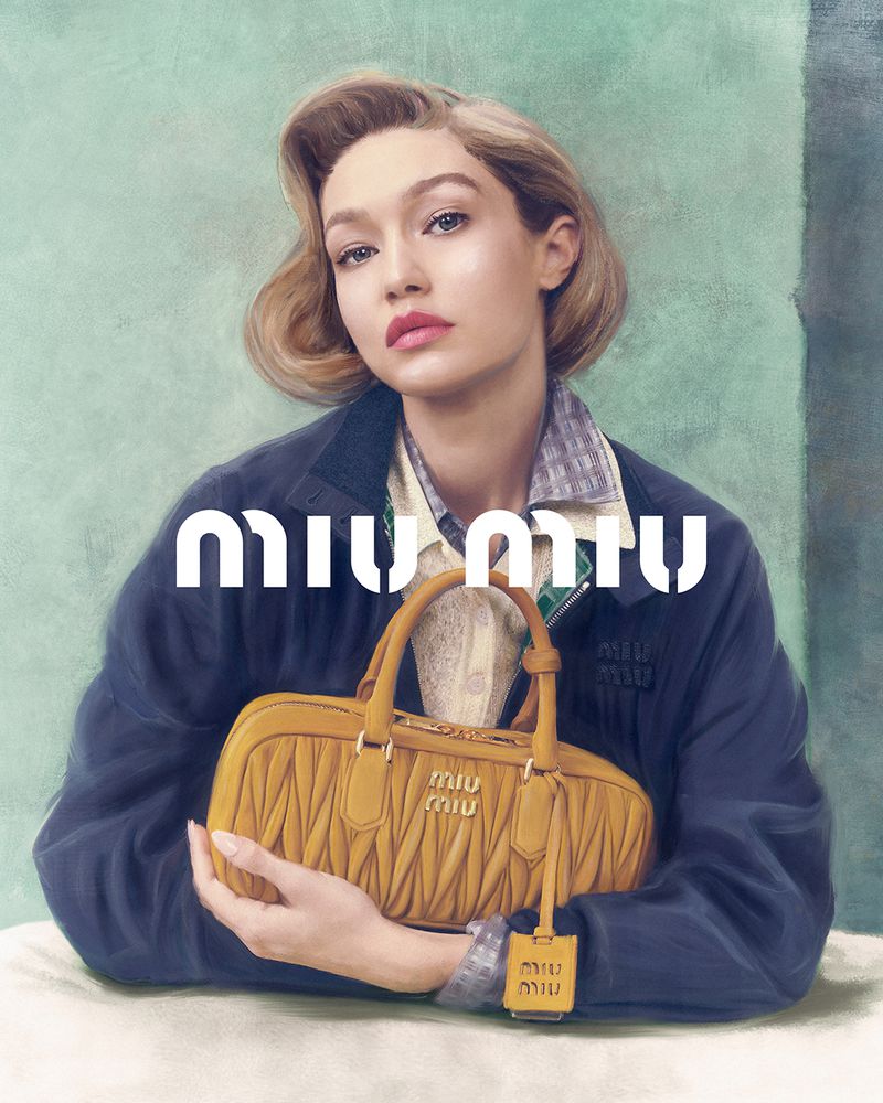 Blonde woman in navy jacket holds a yellow Miu Miu bag in a studio shot against a mottled green backdrop with prominent white logo text.