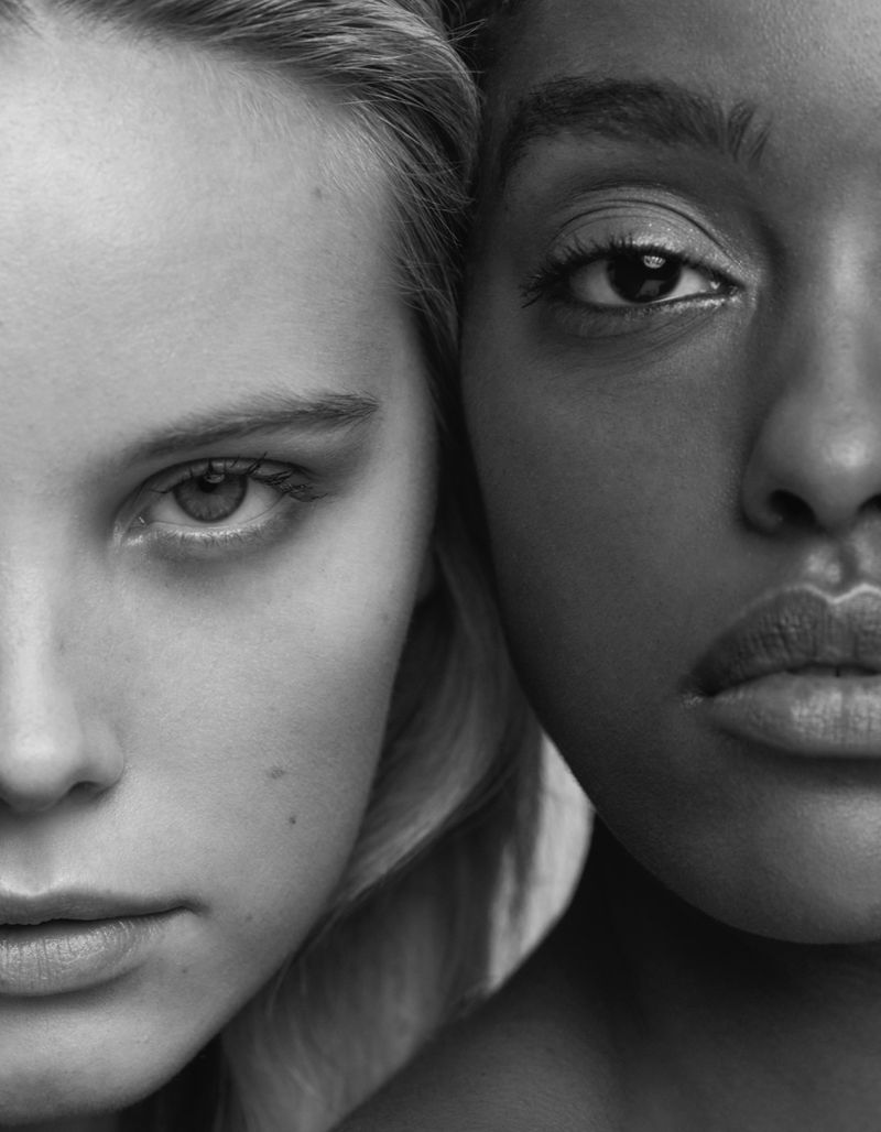 Striking monochrome portrait: Two women of diverse ethnicities, skin tones in stark contrast, faces close, capturing beauty, diversity, and unity.
