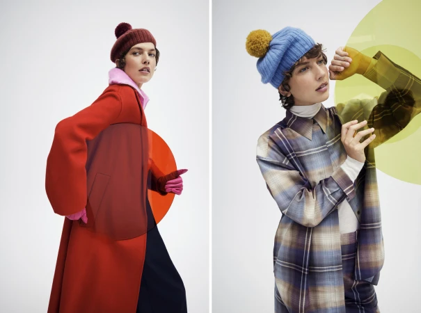 Two women wearing winter hats and colorful coats, posing on a white background with translucent orange and green circles.