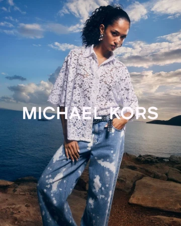Fashion shot of a woman in a white lace top and blue jeans, posing outdoors with a sea and sky background. Designer apparel.