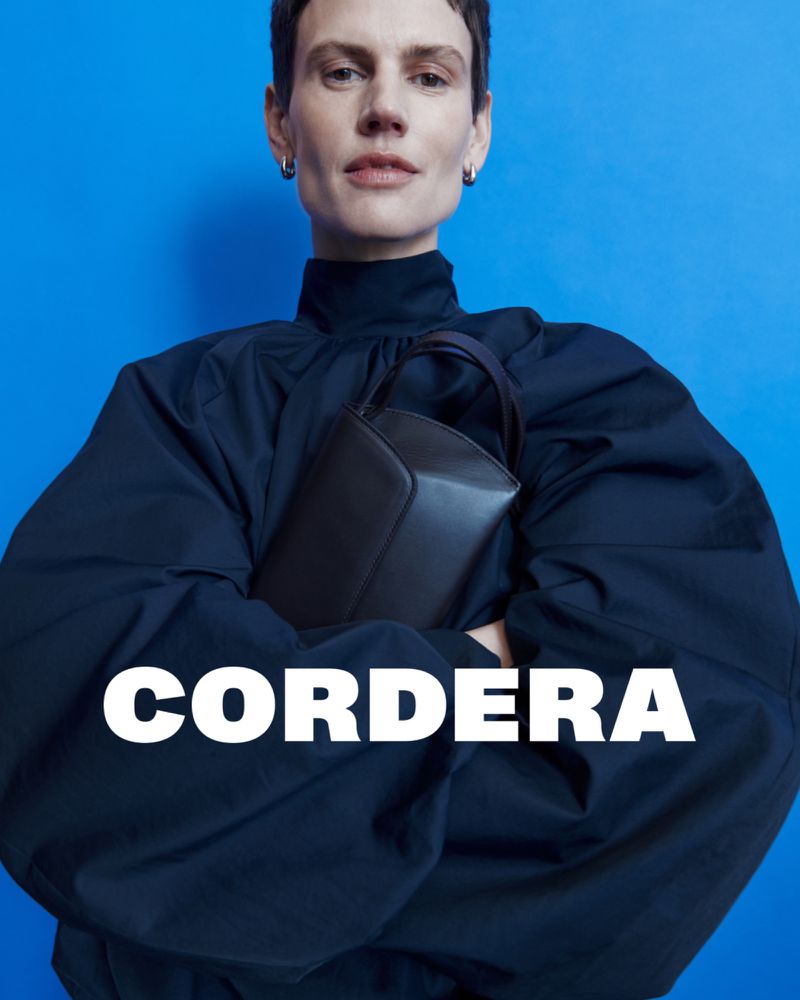 A woman in a navy top holds a dark handbag against a bright blue background, with the brand name 'Cordera' overlaid in white.