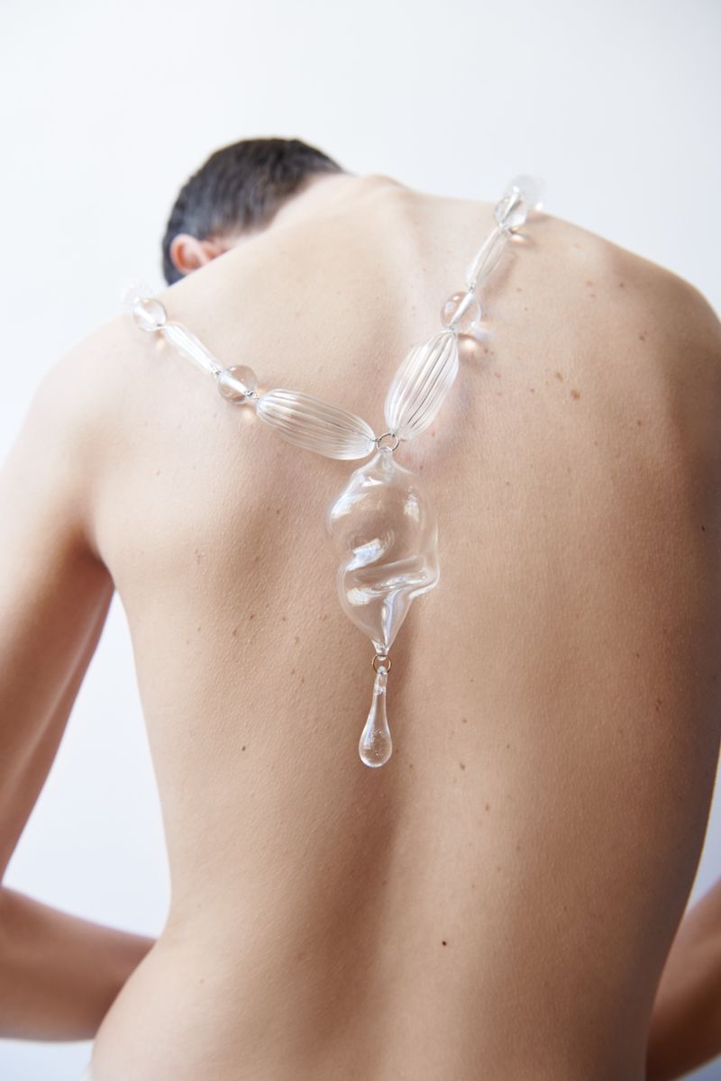 Model seen from behind wearing a large clear glass statement necklace against a bright white background