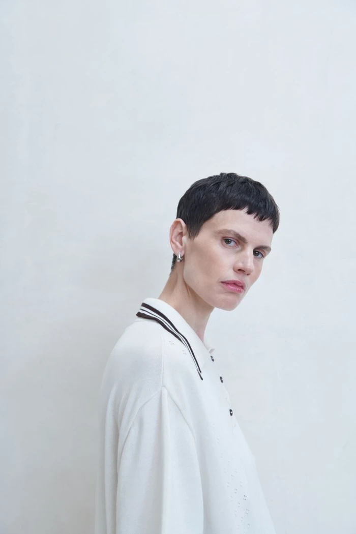 Model with short dark hair wearing a white collared shirt against a plain light wall background for Cordera SS25 campaign