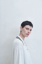 Model with short dark hair wearing a white collared shirt against a plain light wall background for Cordera SS25 campaign