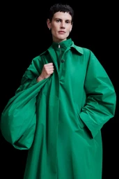 Model wearing a vibrant green coat and holding a matching green shoulder bag against a solid dark background