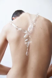 Model seen from behind wearing a large clear glass statement necklace against a bright white background
