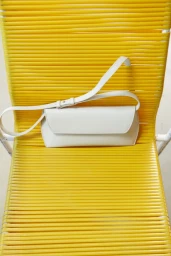 White leather shoulder bag resting on a vibrant yellow corded outdoor chair