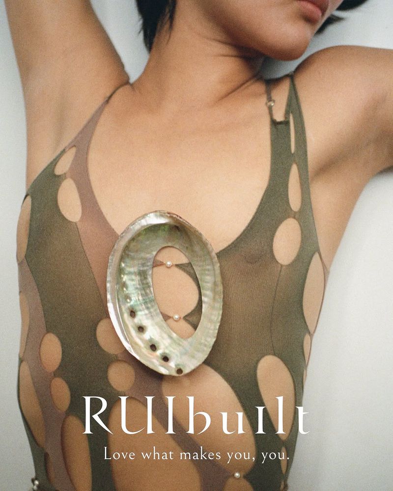 Adult female reclines wearing a light green top with cut-out designs, adorned with pearl accents and a large abalone shell necklace.