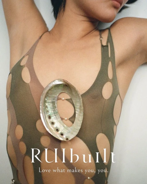 Adult female reclines wearing a light green top with cut-out designs, adorned with pearl accents and a large abalone shell necklace.