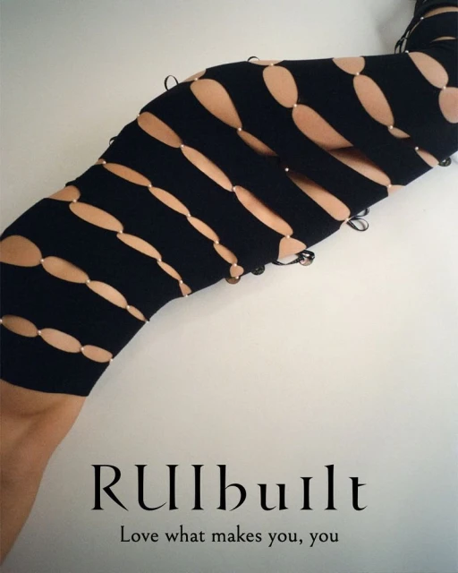 Close-up of a person's lower body and legs wearing a black cut-out dress against a neutral wall, showcasing a unique fashion design.