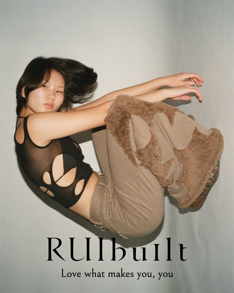 Young Asian woman models a black cutout top and tan pants in a fashion studio shot. The text "RUIbuilt, Love what makes you, you" is displayed.