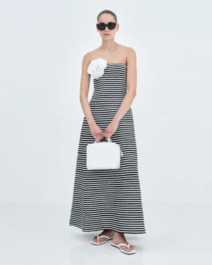 Model wearing a black and white striped strapless maxi dress and sunglasses holding a white handbag against a seamless white background.