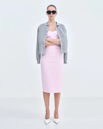 Model wearing a pink midi dress, grey cardigan, pearl necklace and black sunglasses standing against a white seamless background.
