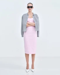 Model wearing a pink midi dress, grey cardigan, pearl necklace and black sunglasses standing against a white seamless background.
