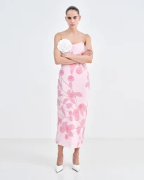 Model wearing a pink floral slip dress with a large white fabric flower detail against a white background