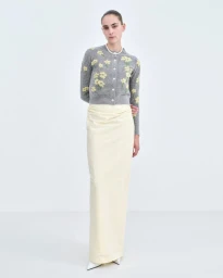 Model wearing a grey floral cardigan and long cream skirt standing against a white seamless background