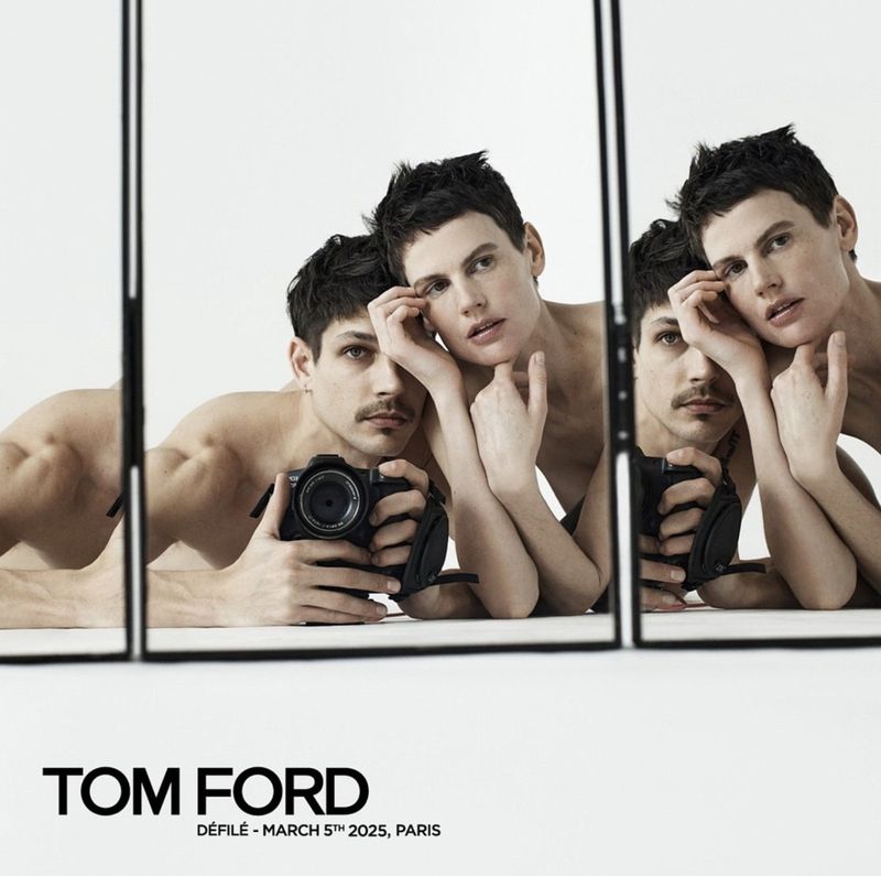 Fashion shot with two men reflected in a segmented mirror, one holding a camera, set against a stark white backdrop, featuring a Tom Ford logo.