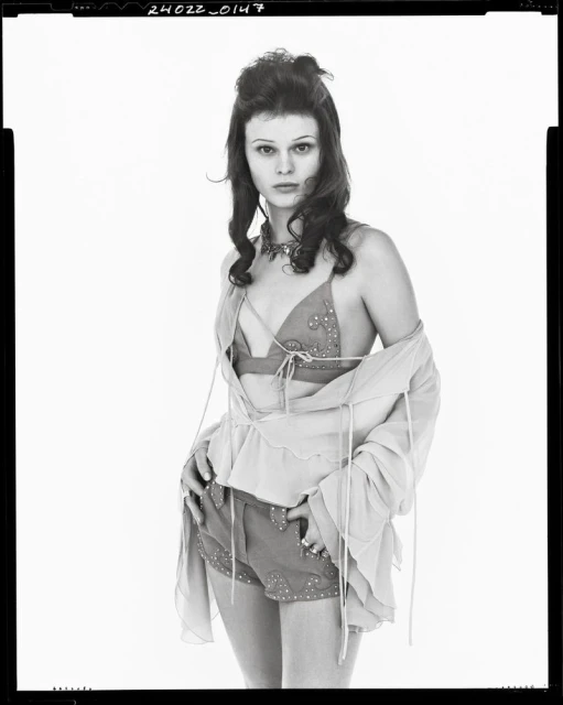 Monochrome portrait of a fair-skinned woman with curly dark hair, wearing a beaded top and shorts, and a sheer open blouse.