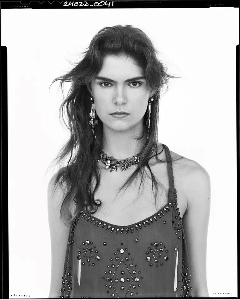 Portrait of a female model wearing embellished dress and statement jewelry against a plain background