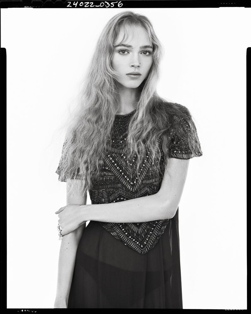 Black and white portrait of a female model wearing an embellished short-sleeve dress against a plain white background.