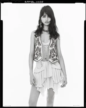 Model wearing an embroidered vest and layered skirt against a white studio background with black film border framing.