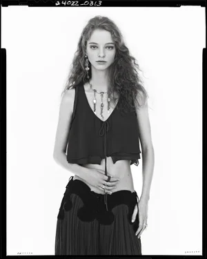 Model in black sleeveless top and dark skirt wearing layered pendant necklace against a white background