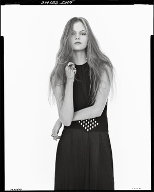 Model in a black dress with studded belt and rings against a white seamless background