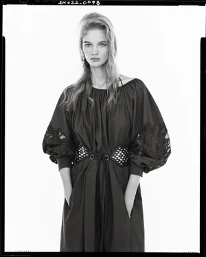 Portrait of a female model wearing a dark gathered dress with puffed sleeves and a wide cutout belt against white