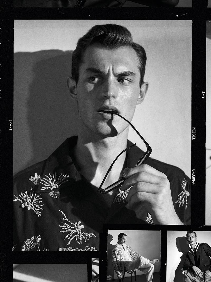 Monochrome portrait of a handsome male model indoors, wearing a patterned shirt and holding glasses in his mouth, studio lighting.