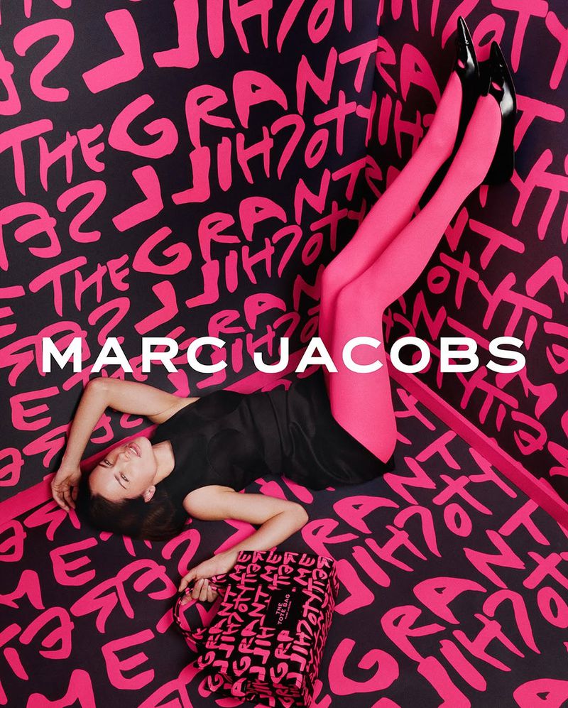 Fashion model poses with a Marc Jacobs handbag in a stylized pink-and-black studio setting with graffiti-style lettering.