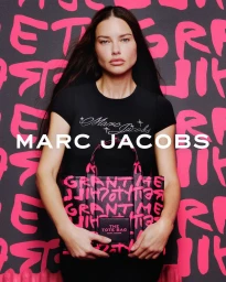 Model Adriana Lima holding a pink and black graffiti tote bag in front of a matching typographic backdrop for Marc Jacobs.